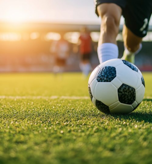 Soccer player kicking the ball on green grass, close-up of foot and soccer ball with motion blur, stadium in the background, action shot, blurred players in the background